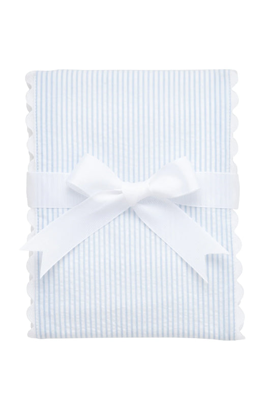White burp cloth trimmed in light-blue seersucker stripe with ric rac edge, folded and tied with a white bow against a white background.